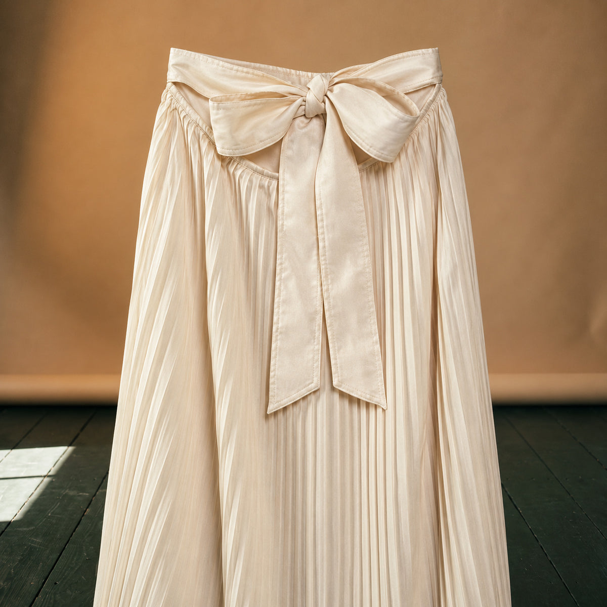 Gros plan sur le plissé fin, la ceinture élastique et le nœud de la jupe longue années 80 plissée beige Image
